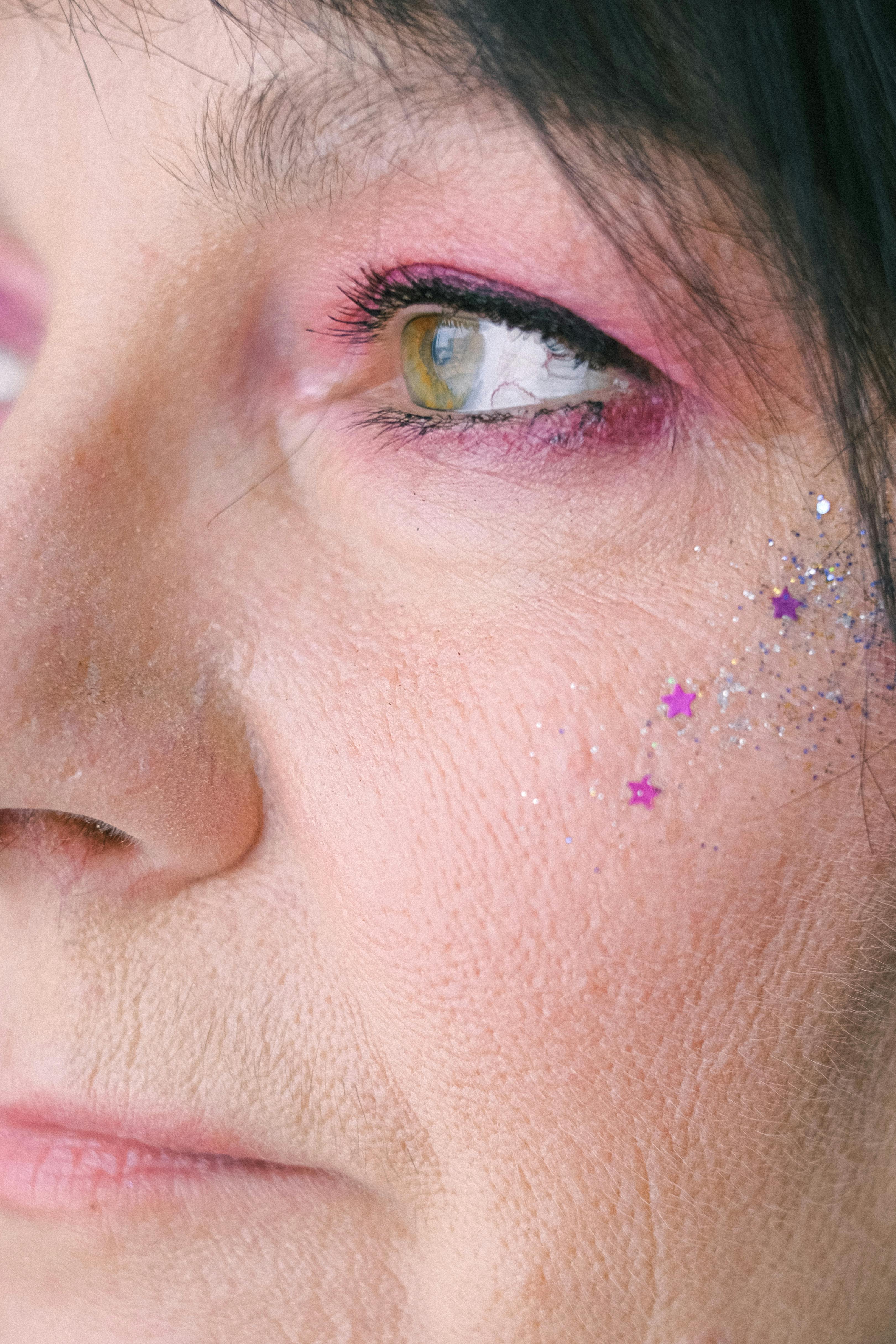 Detailed headshot of an elderly woman wearing eye makeup and glitter stars.