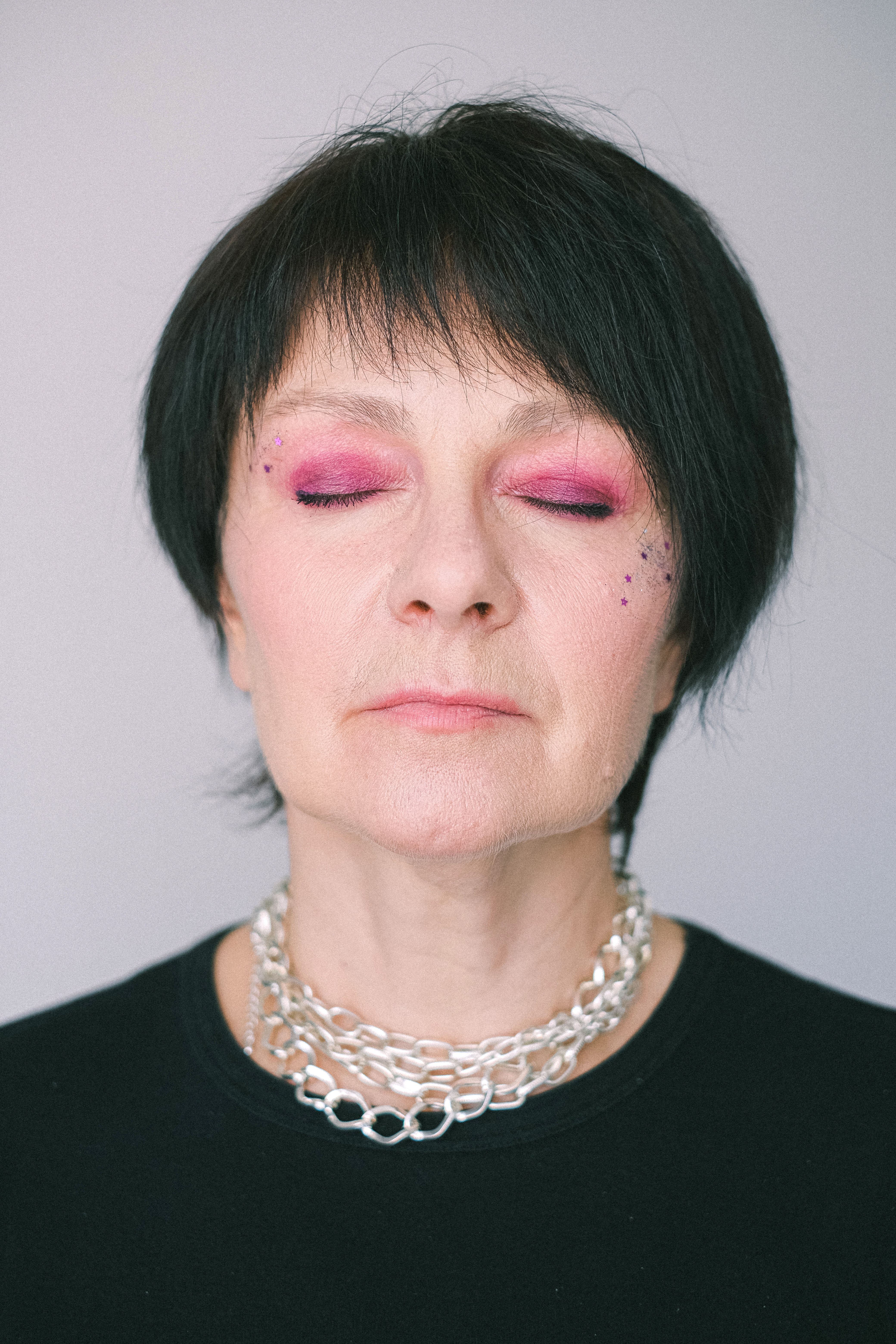 Close-up portrait of a woman with vibrant pink makeup, eyes closed, and silver jewelry.