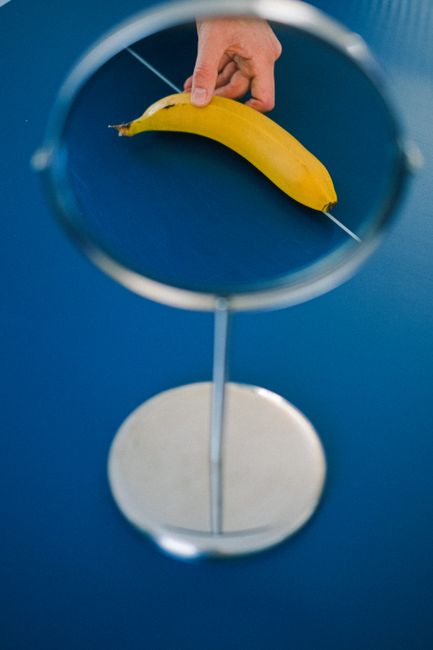 A hand holds a banana reflected in a mirror on a blue surface.