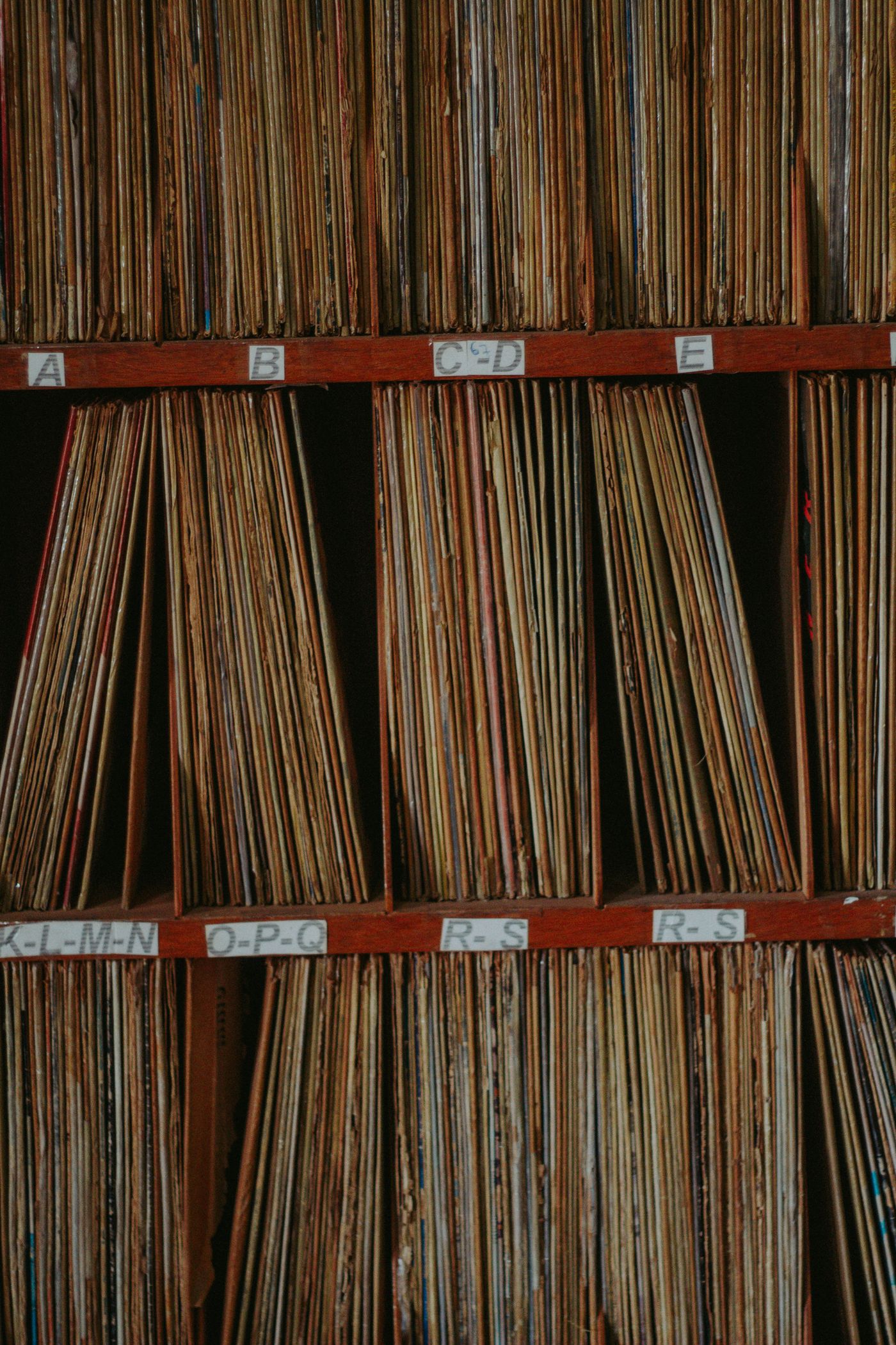 Densely packed rows of filed folders on wooden shelves behind alphabetical divider labels reading K-L-M-N, O-P-Q and R-S
