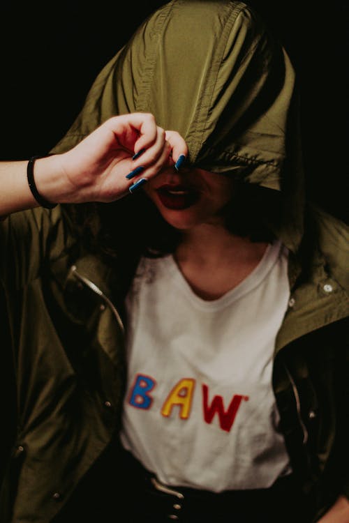 Young faceless female with red lips covering face with hood from outwear while sitting alone