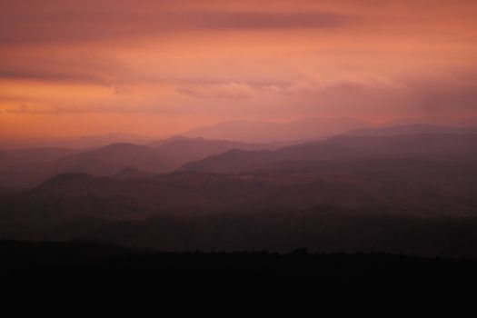 A tranquil scene of mountain ranges under a warm, colorful sunset sky.