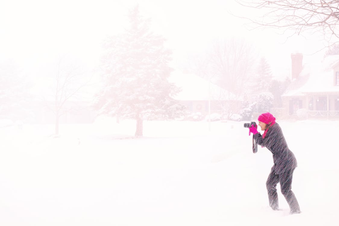 Mulher Vestida Com Um Hijab Rosa Segurando Uma Câmera Dslr Preta Sob A Neve Violenta Durante O Dia