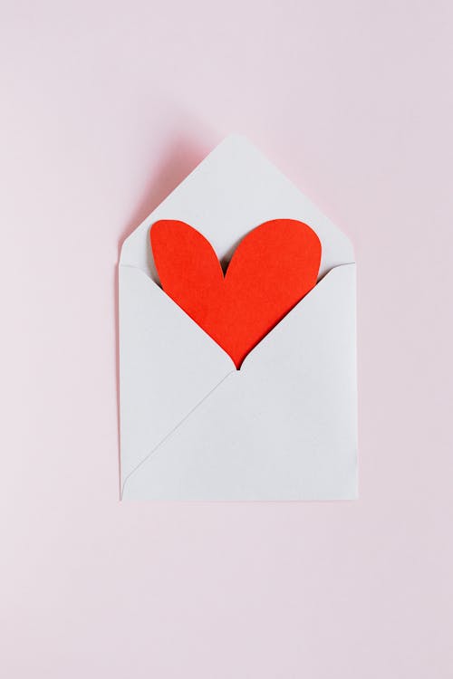 Free Top view of opened white envelope with handmade red paper heart placed against pink background as gift for Valentine day Stock Photo