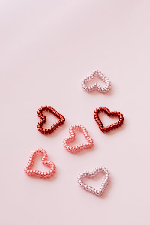 Free Top view of multicolored coil hair ties in shape of hearts composed on pink surface for Saint Valentines Day Stock Photo