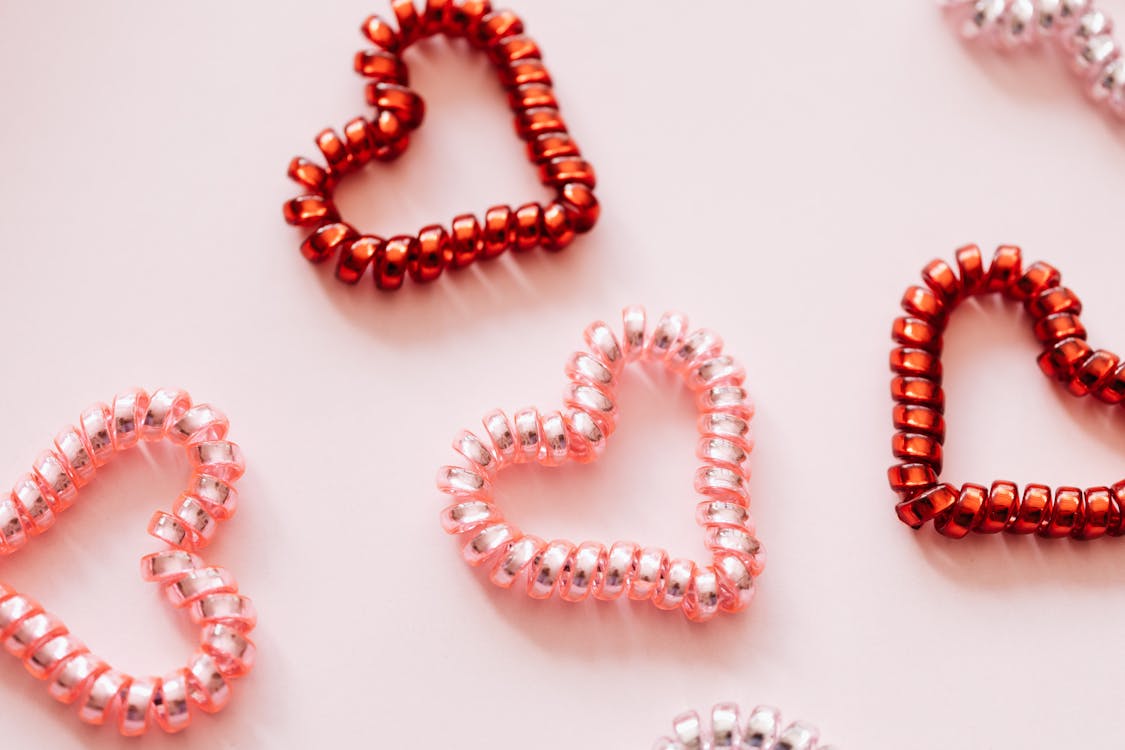 Colorful hair ties in shape of hearts on pink surface · Free Stock Photo