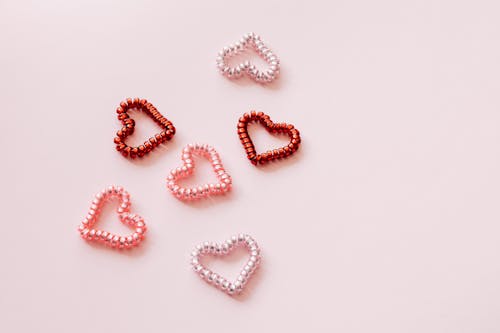 Top view of composition of small multicolored decorative hearts made of shiny pearl globules on pale pink surface