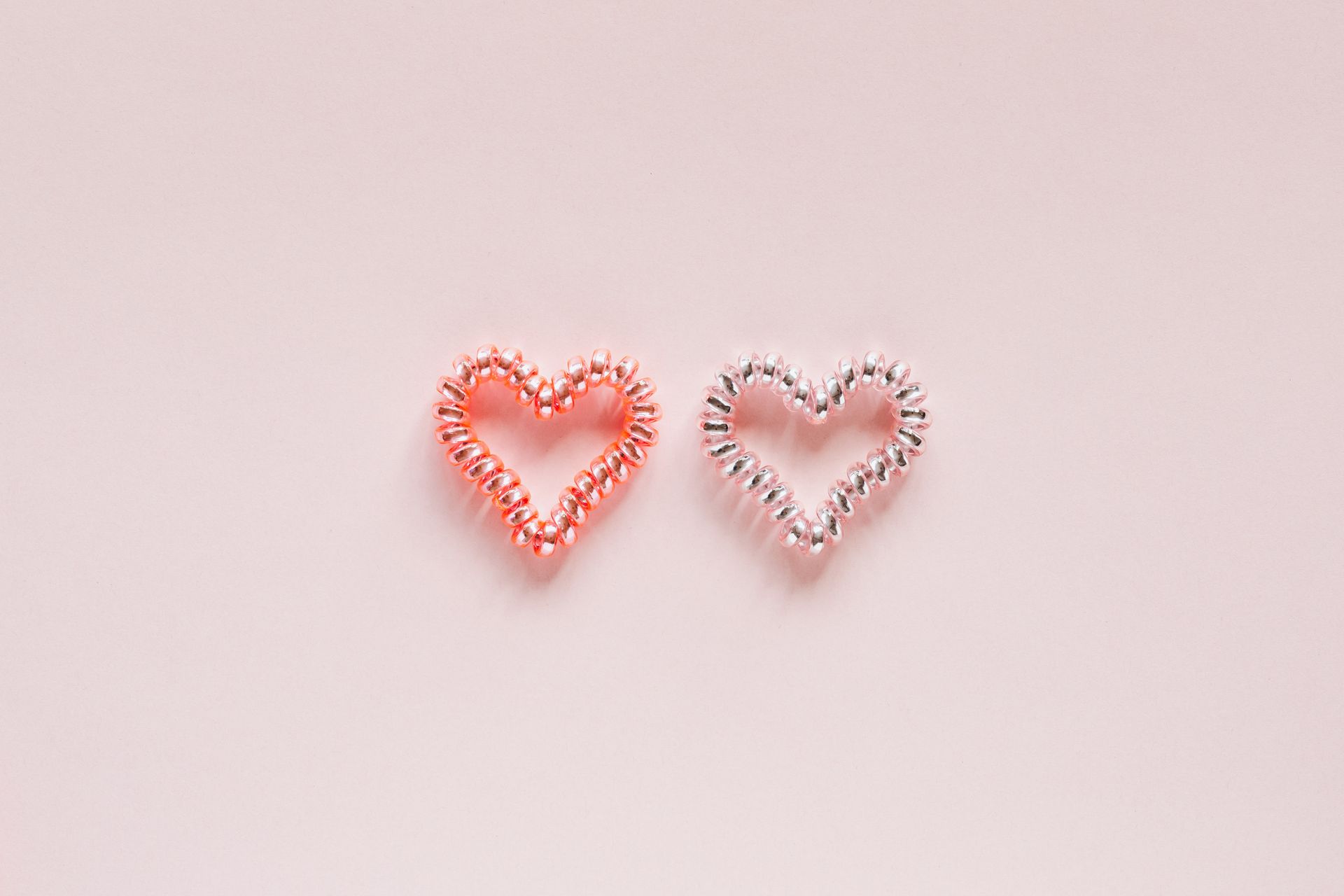 From above of pair of small brilliant hearts made of elastic hair ties on pale pink surface