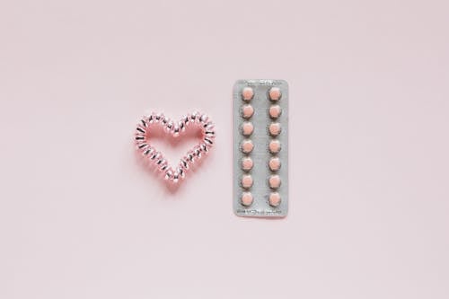Free From above of whole blister of pills and shiny handmade heart of coil hair tie on pink surface Stock Photo