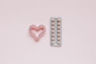 From above of whole blister of pills and shiny handmade heart of coil hair tie on pink surface