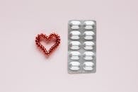 Top view of plastic blister with medical pills placed near red heart made of spiral elastic for hair on pink background