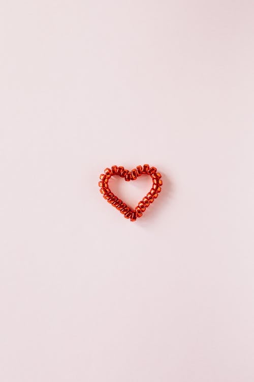 Free Top view of red heart made of spiral elastic for hair placed on pink background Stock Photo