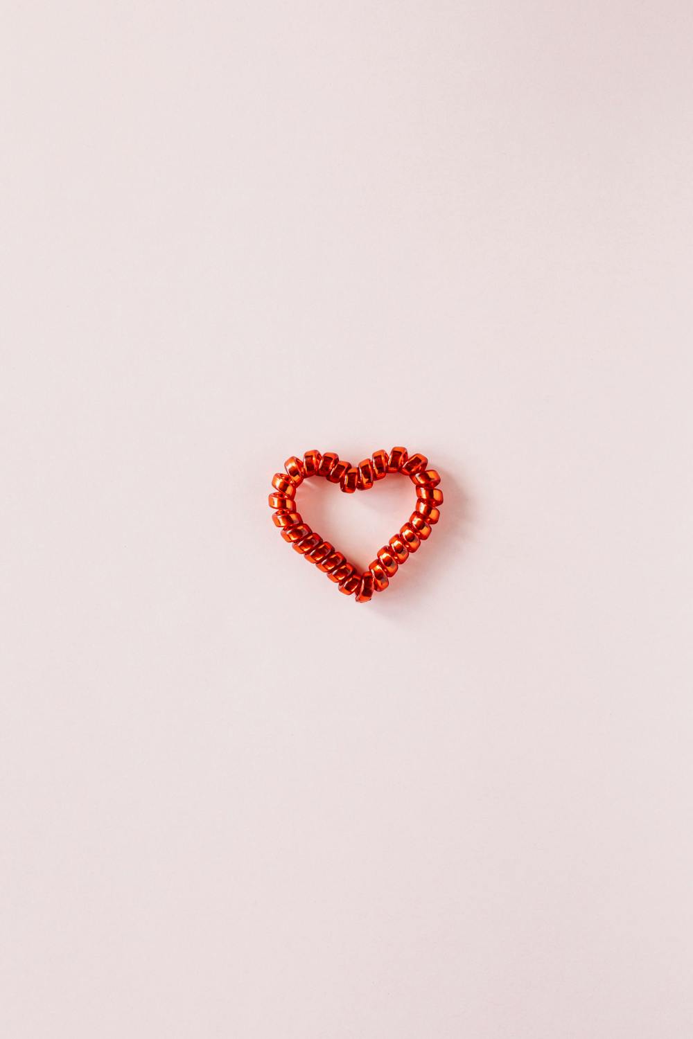 Red heart made of coil hair tie on pink background · Free Stock Photo