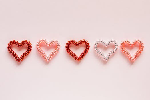 Five heart-shaped spirals arranged creatively on a pink background, perfect for Valentine's Day themes.