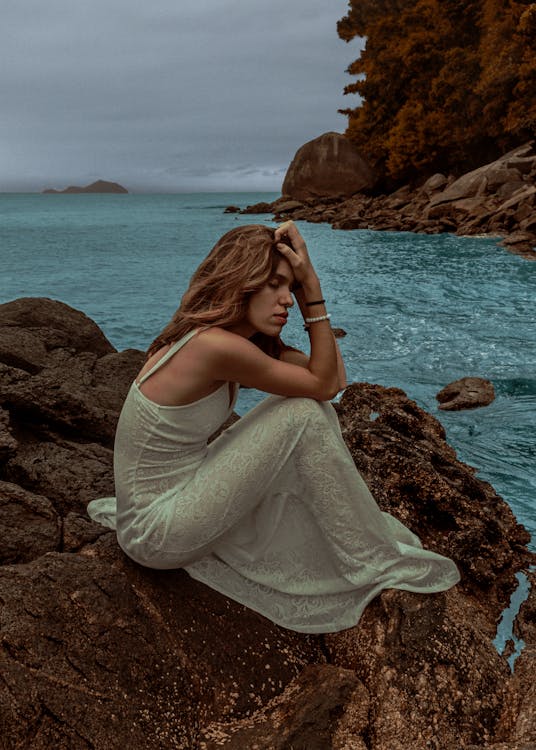Young sad woman sitting on rocky shore