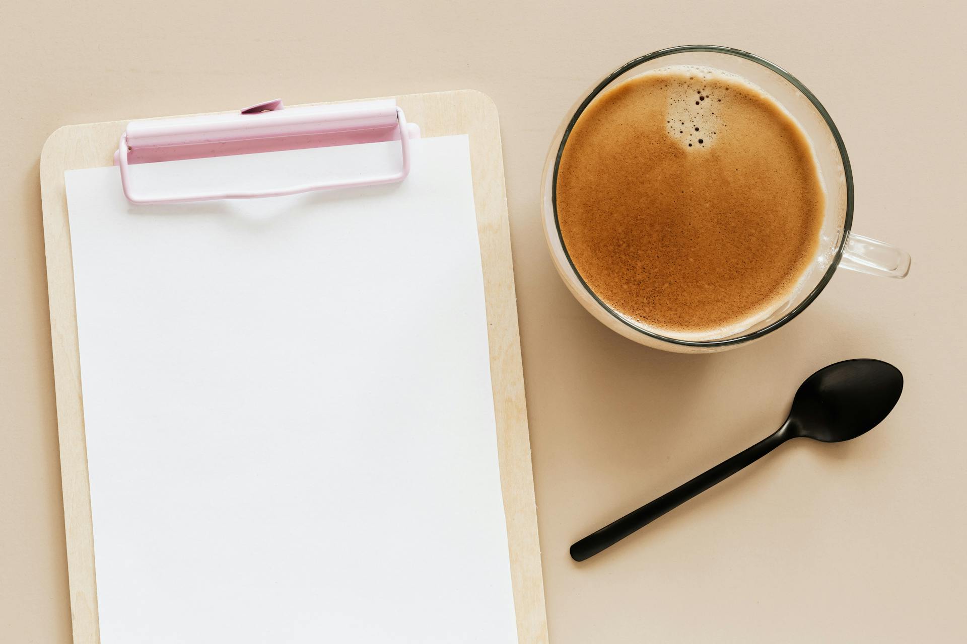 Delicious hot coffee and clipboard on beige surface