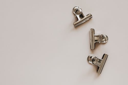 From above of identical metallic clips made of solid material with smooth surface on beige background