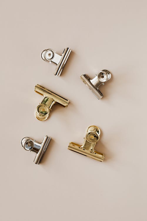From above of set of golden and silver clips made of stainless steel on beige background