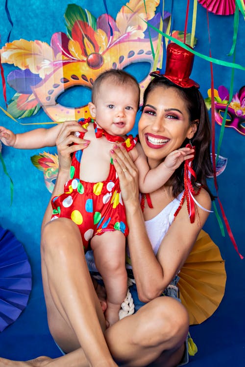 Cheerful young female smiling brightly and holding baby in costume during birthday celebration