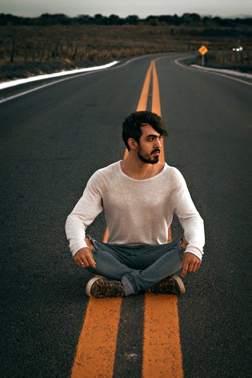 Dreamy ethnic man sitting on asphalt road