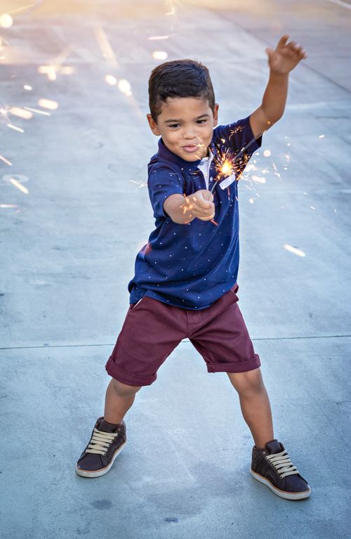 Free From above full body of happy little boy with bright sparkler in hand Stock Photo