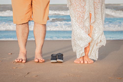 Couple standing on sandy coast with tiny baby boots