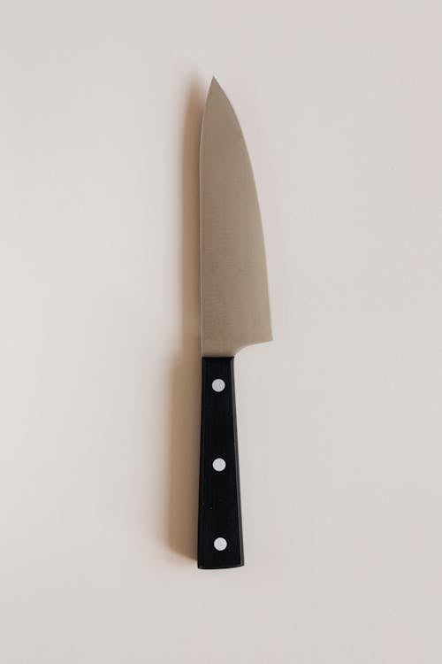 Top view of large black handle knife with sharp blade for cutting products and cooking food placed on gray kitchen table