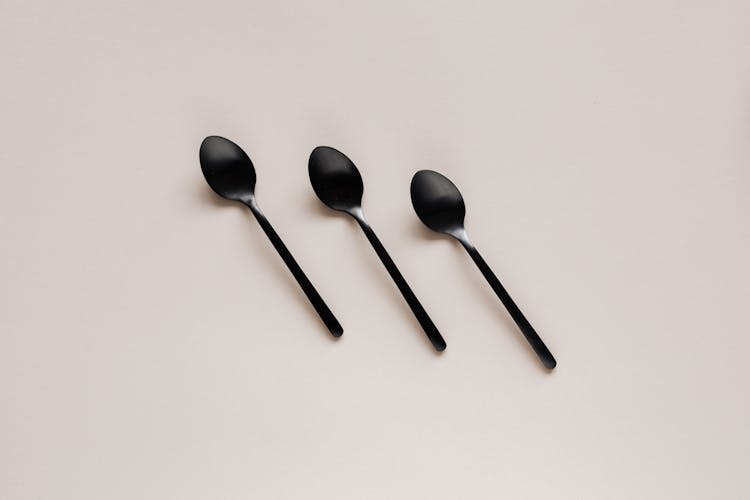 Set Of Shiny Black Spoons On Gray Table