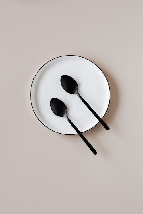 Top view of black teaspoons placed on white ceramic plate with black border served on beige table