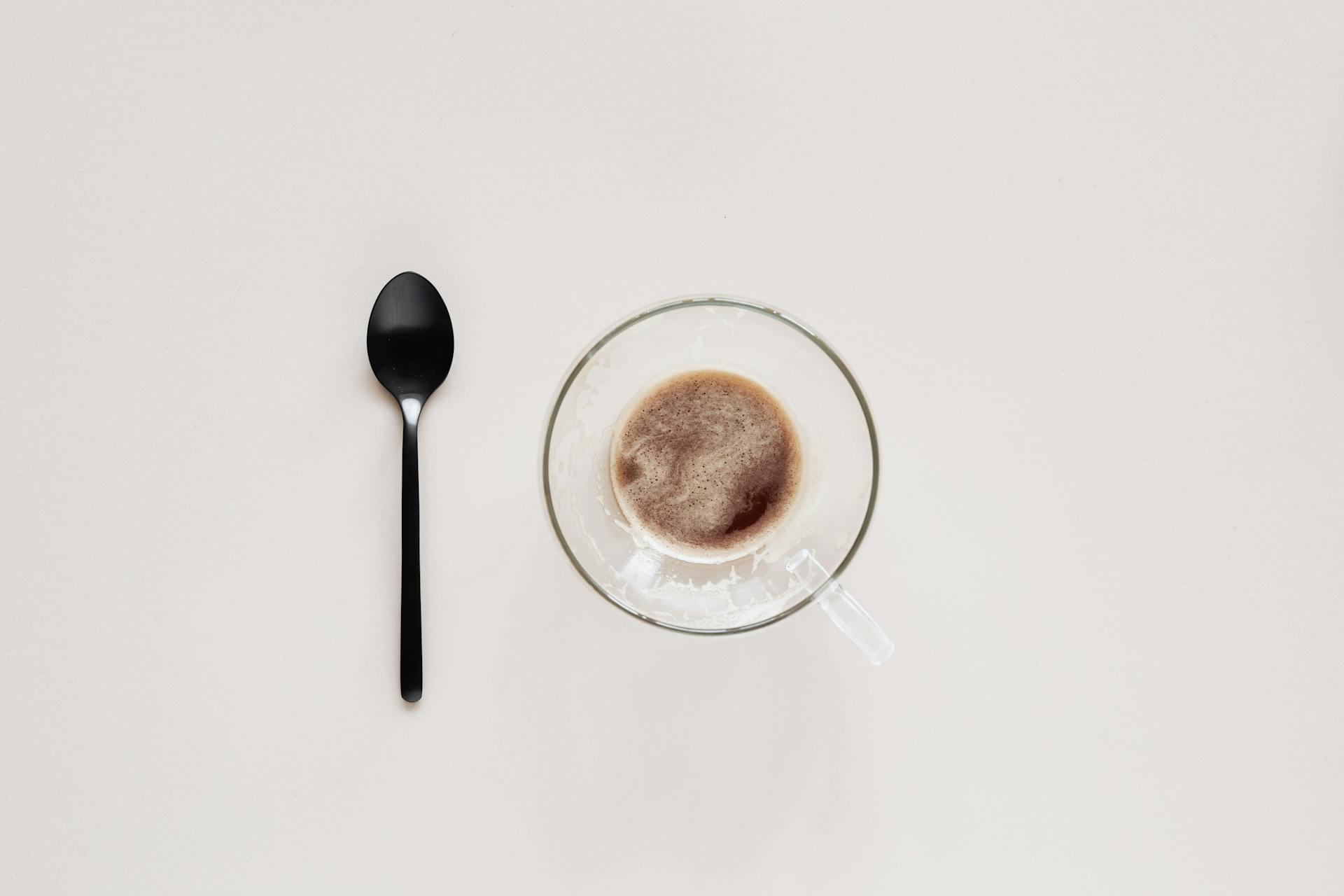 A minimalist flat lay of a coffee cup and black spoon on a beige background, perfect for modern design concepts.