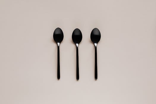 Three black spoons arranged on a beige background in a minimalist flat lay style.