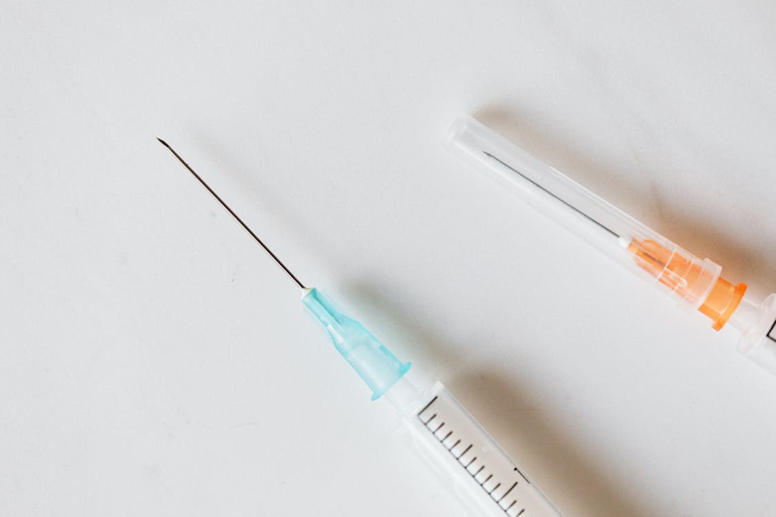 Free From above of medical syringe with needle placed near syringe with covered needle on white table Stock Photo