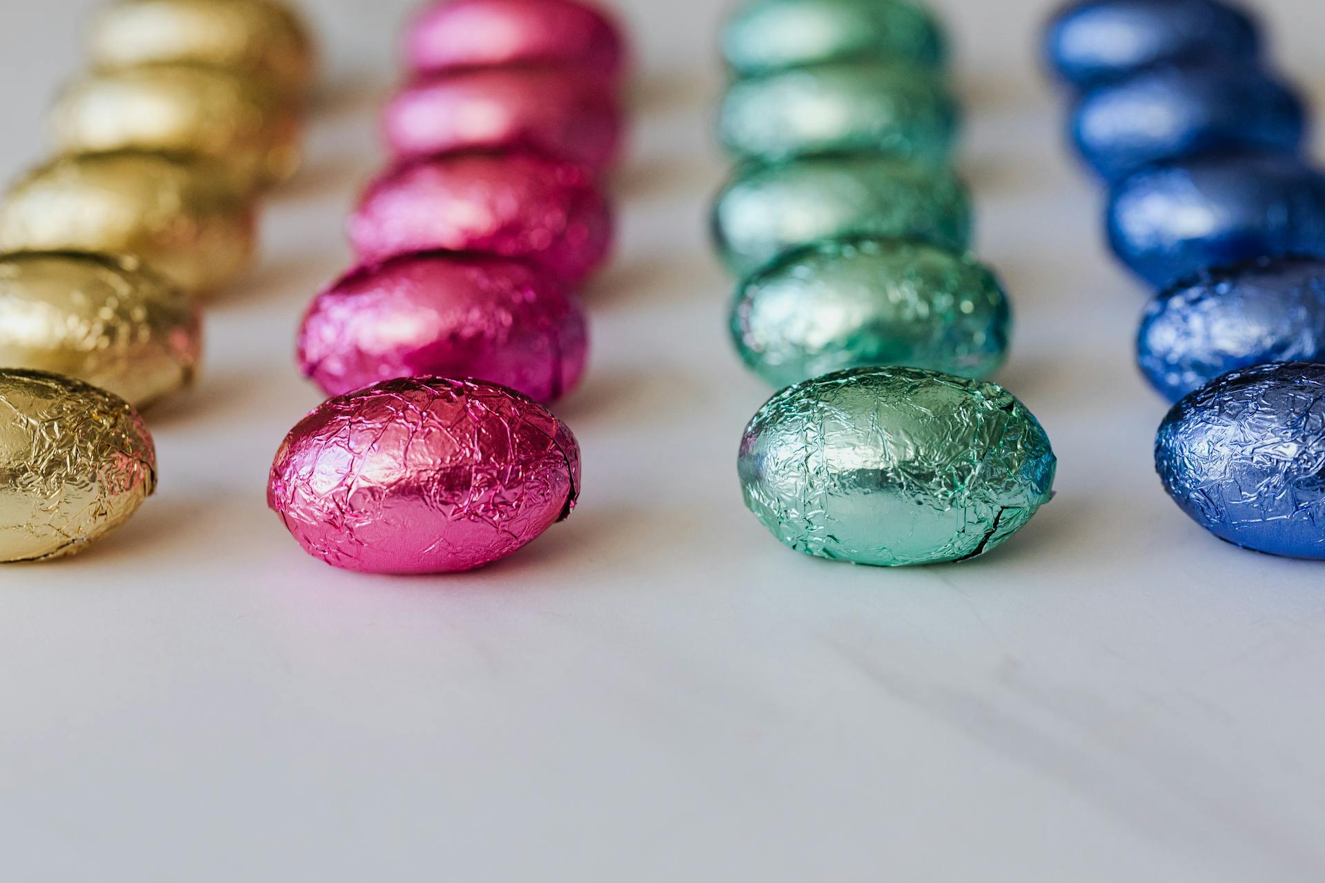 Vibrant foil wrapped chocolate eggs in colorful rows on a white background, perfect for Easter themes.