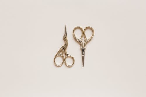 Top view composition of scissors of various shape with carved ornament on beige table