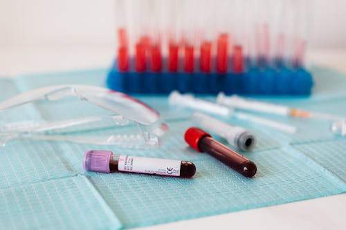 Free Closeup of full vials of blood placed on medical diaper near plastic eyeglasses and syringes and test tubes in container Stock Photo