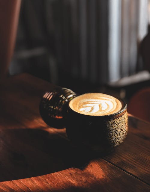 From above of mug of hot aromatic cappuccino placed on lumber table at sunlight