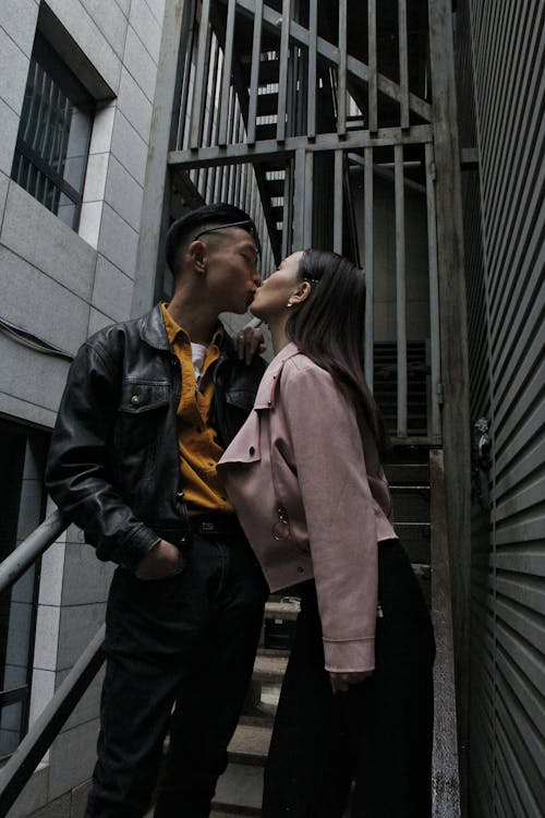 From below of Asian romantic trendy couple kissing each other while spending time together