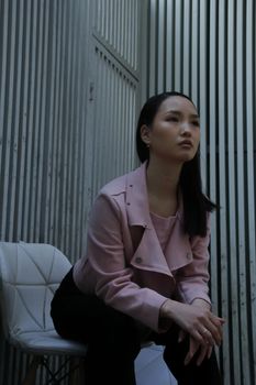 Low angle of young Asian female with makeup leaning forward while sitting on chair on street