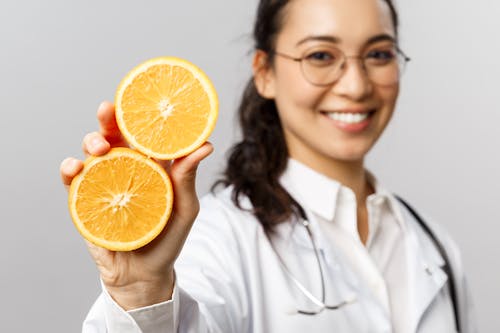 Woman in White Dress Shirt Holding Sliced Orange Fruit
