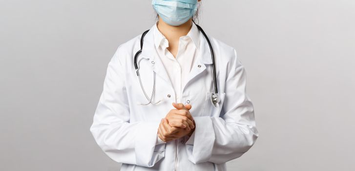Healthcare professional wearing a mask and lab coat with stethoscope in neutral background.