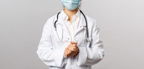 Free Healthcare professional wearing a mask and lab coat with stethoscope in neutral background. Stock Photo