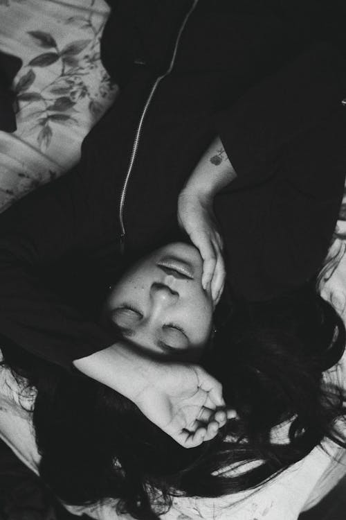 Free Black and white of upside down young female touching face while resting on bed Stock Photo