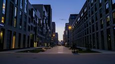 Empty pedestrian street with benches between stylish modern geometric buildings against sunrise sky