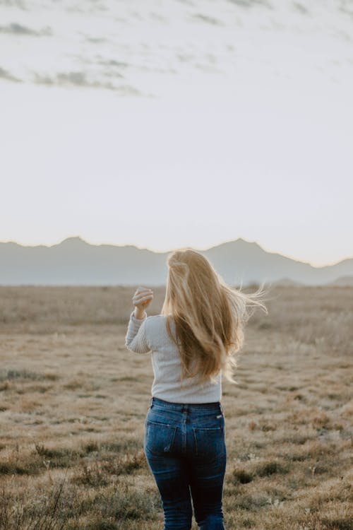 Woman in White Long Sleeve Shirt and Denim Jeans Standing on Grass Field