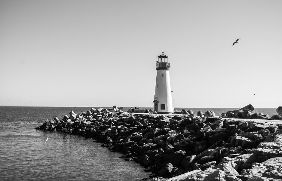 A serene black and white photo of a lighthouse surrounded by rocks and ocean.