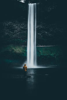 Person in yellow coat admiring a stunning waterfall, a perfect exploration background.