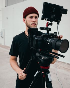A male filmmaker uses professional equipment outdoors, capturing visual content.