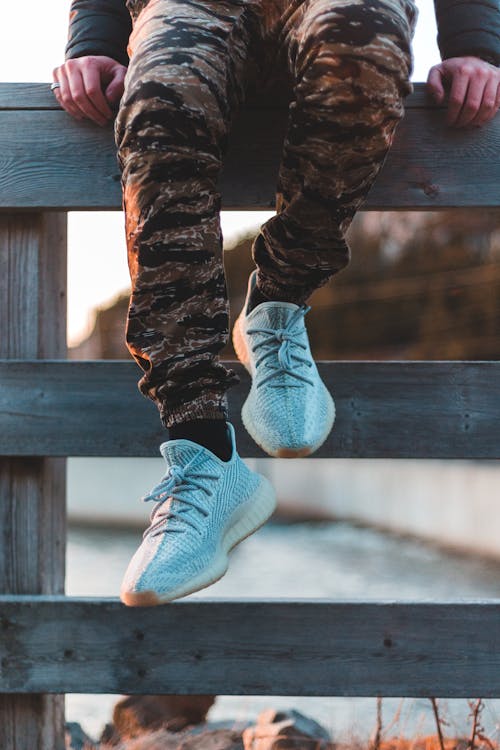 Crop person in stylish sneakers on fence