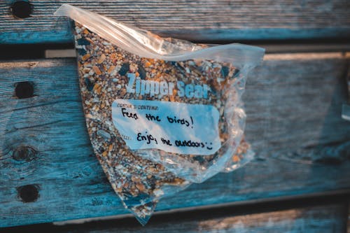 From above of transparent plastic zipper bag with bird feed and titles on wooden plank