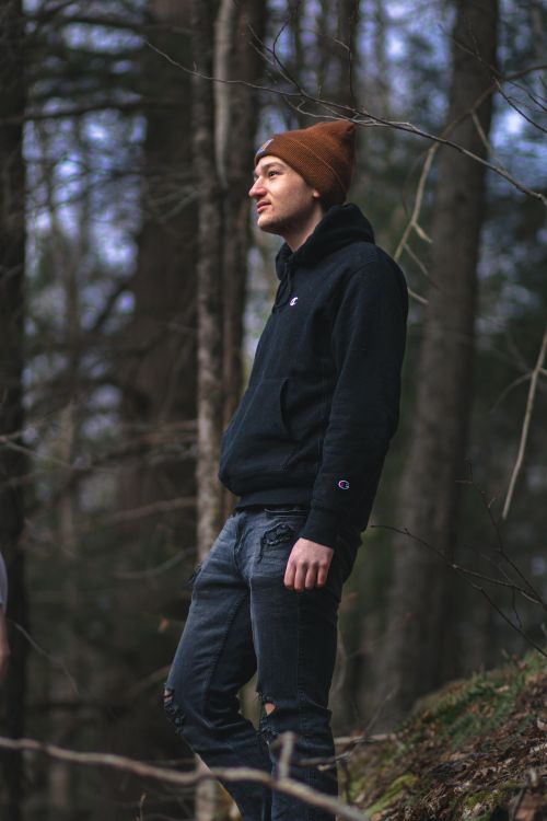 Free Side view of young dreamy male in trendy wear and knitted hat admiring autumn woods while looking away Stock Photo